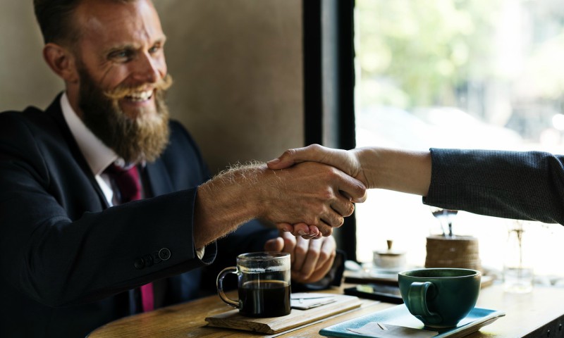 sales person smiling and shaking hand after closing the deal and winning the client